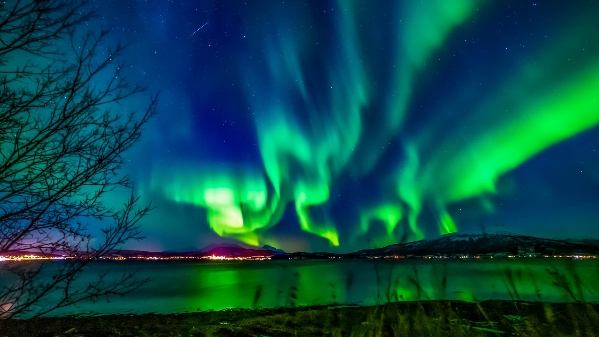 Bright green Northern Lights above the water and city lights of Tromsø
