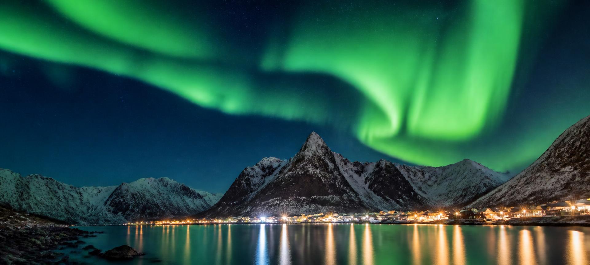 Green aurora over a snow-covered Norwegian fjord landscape